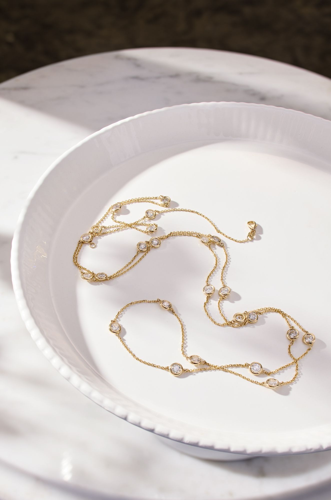 A fine gold station necklace laid on a white porcelain dish