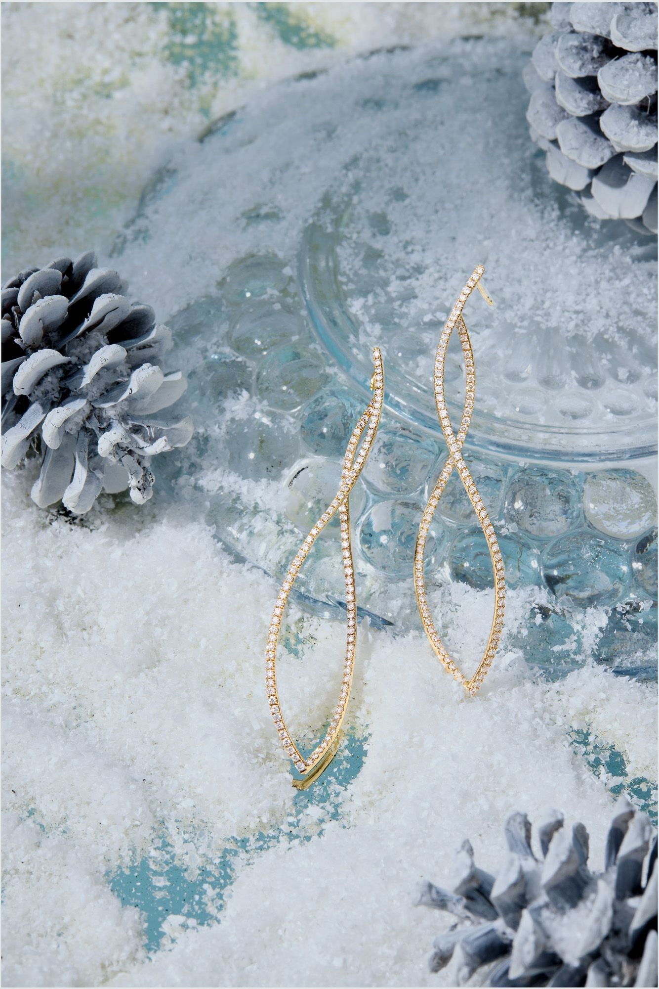 Gold drop earrings photographed on snow with pine cones