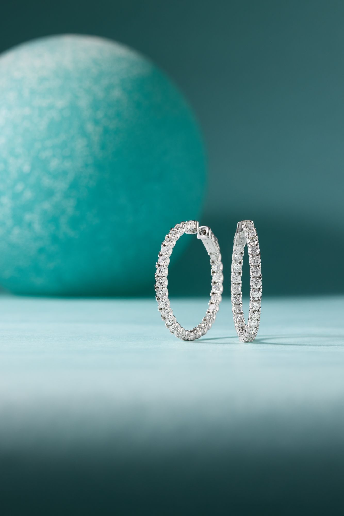 Diamond hoop earrings photographed against a pale teal sphere